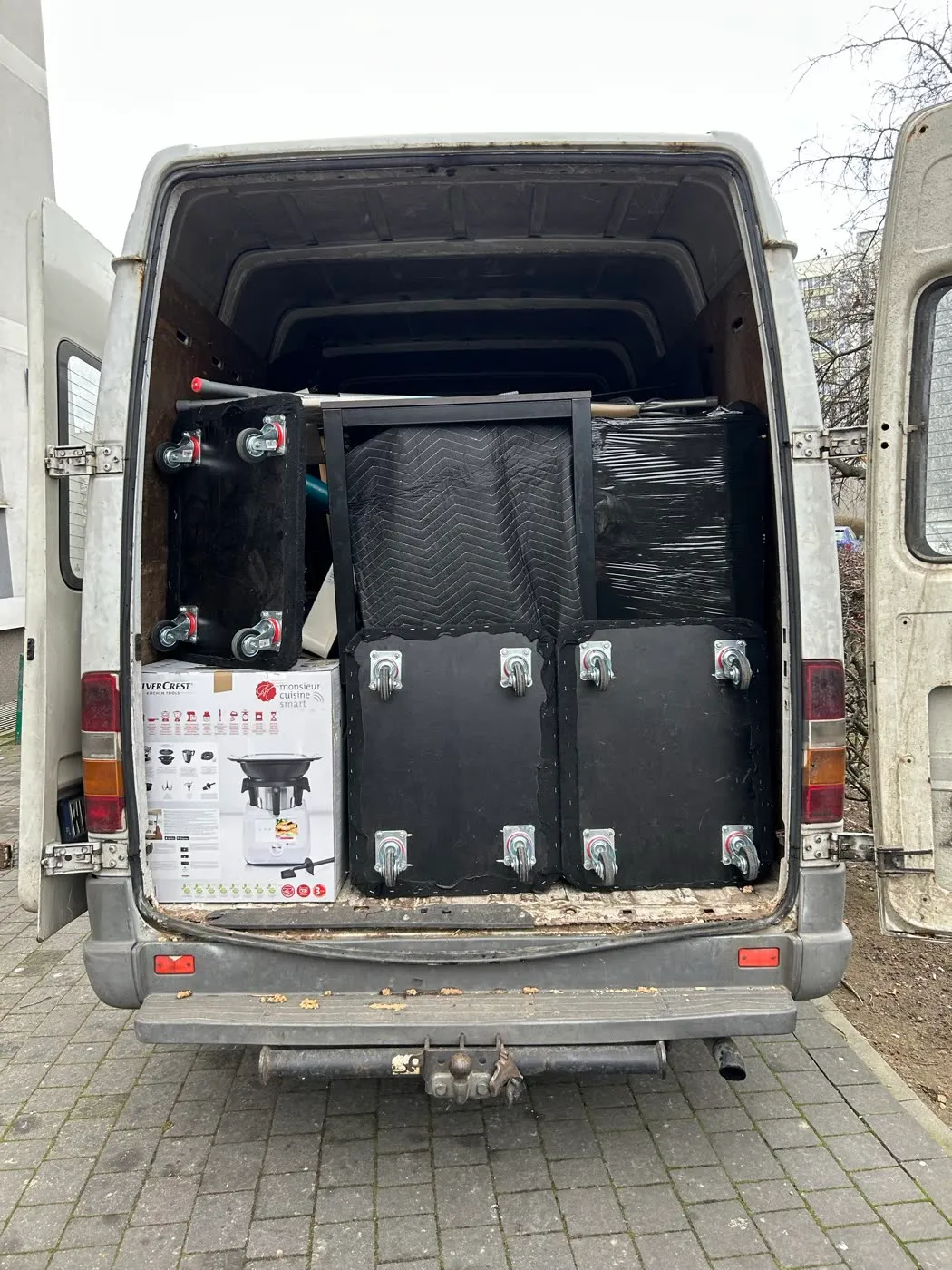 Otwarty kufer busa z platformami transportowymi na kółkach i meblami pod kocami