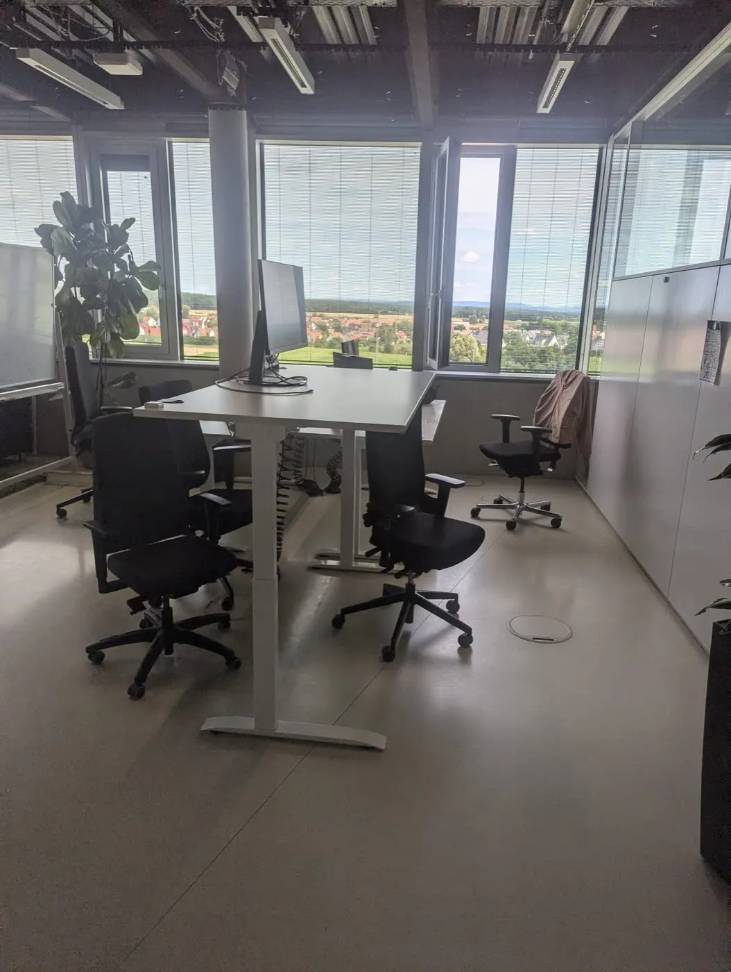 Biurko z monitorem i trzy fotele biurowe ustawione w pomieszczeniu z panoramicznym oknem