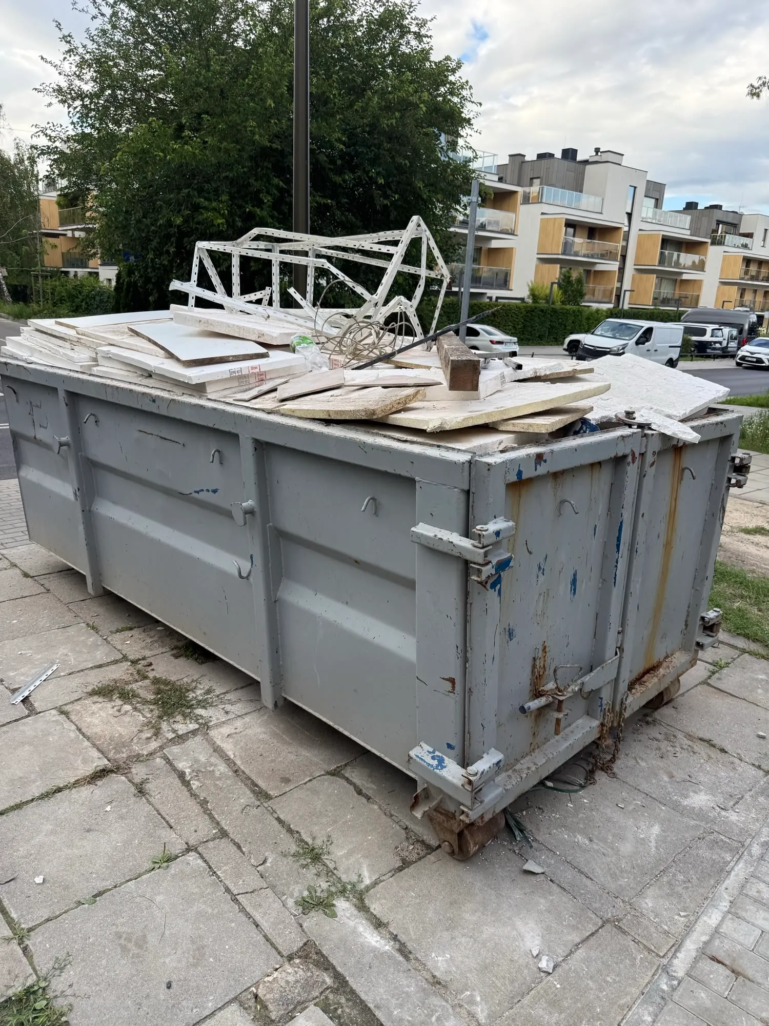 Kontener na gruz ustawiony na chodniku, wypełniony odpadami budowlanymi