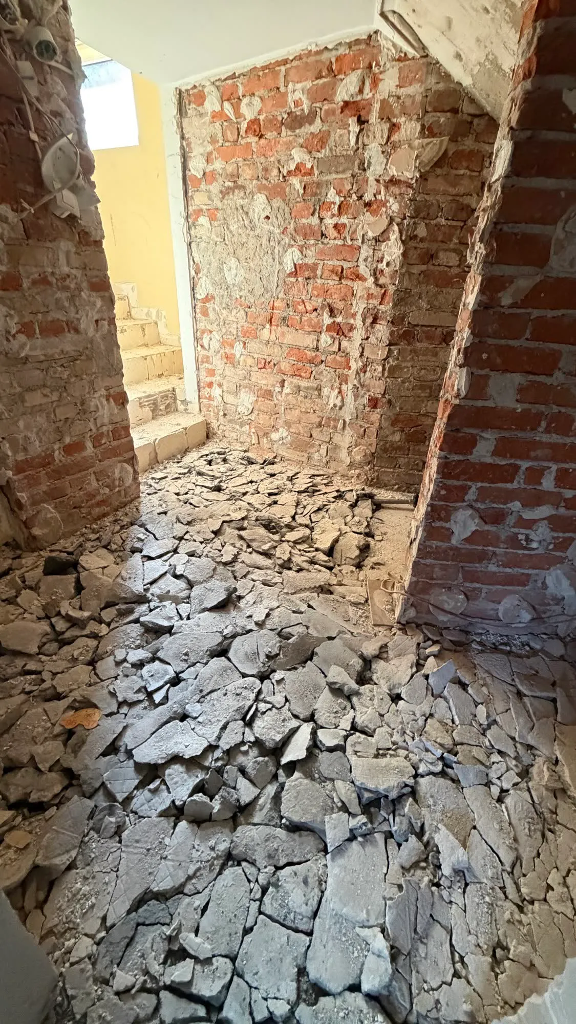 Skuta posadzka i gruz na podłodze między odsłoniętymi ścianami z cegły