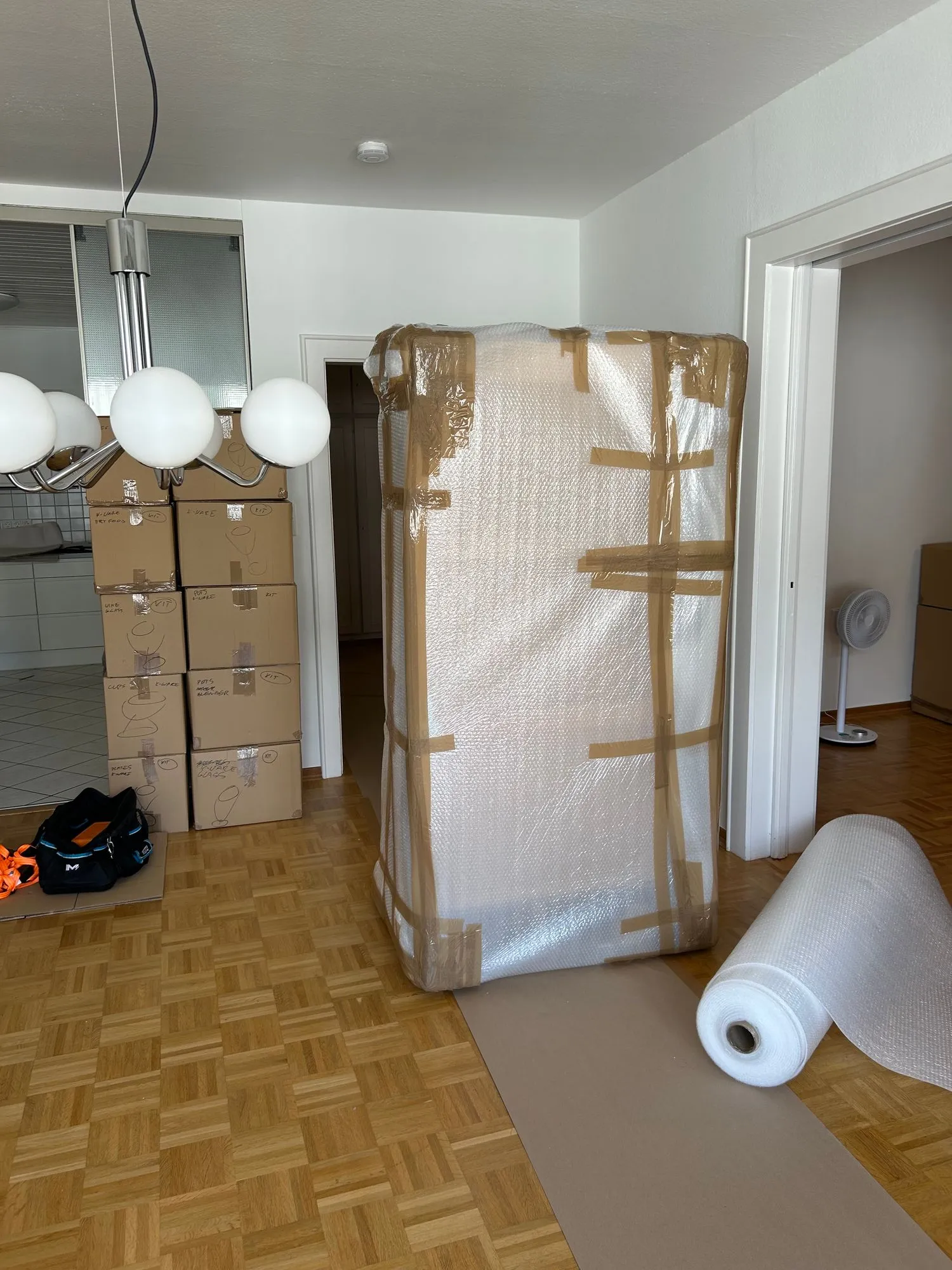 Wysoki mebel owinięty folią bąbelkową, obok spakowane kartony, na podłodze rozłożona mata ochronna