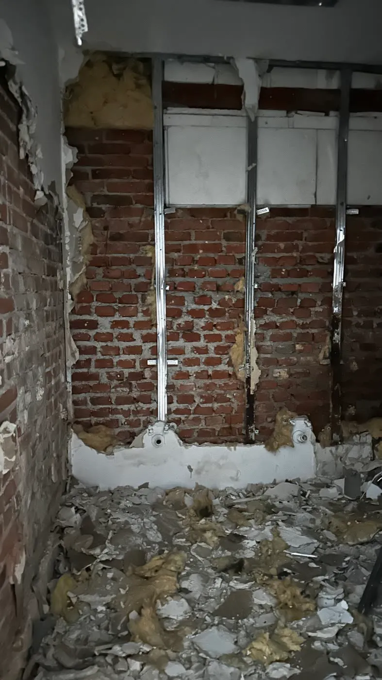 Odsłonięta ceglana ściana ze stalowymi profilami stelaża po zdjęciu zabudowy z płyt, gruz na podłodze