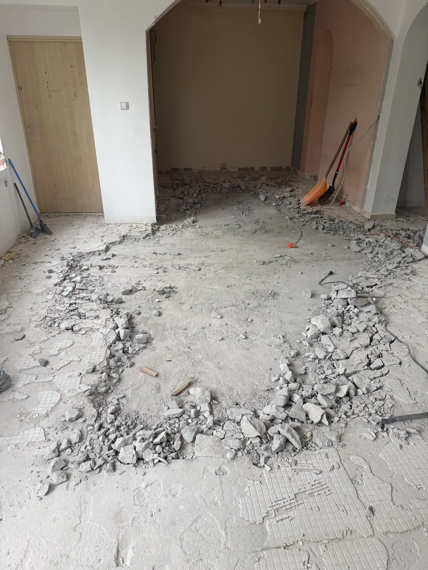 Pokój w trakcie skuwania wylewki, rozkruszony beton i narzędzia na podłodze