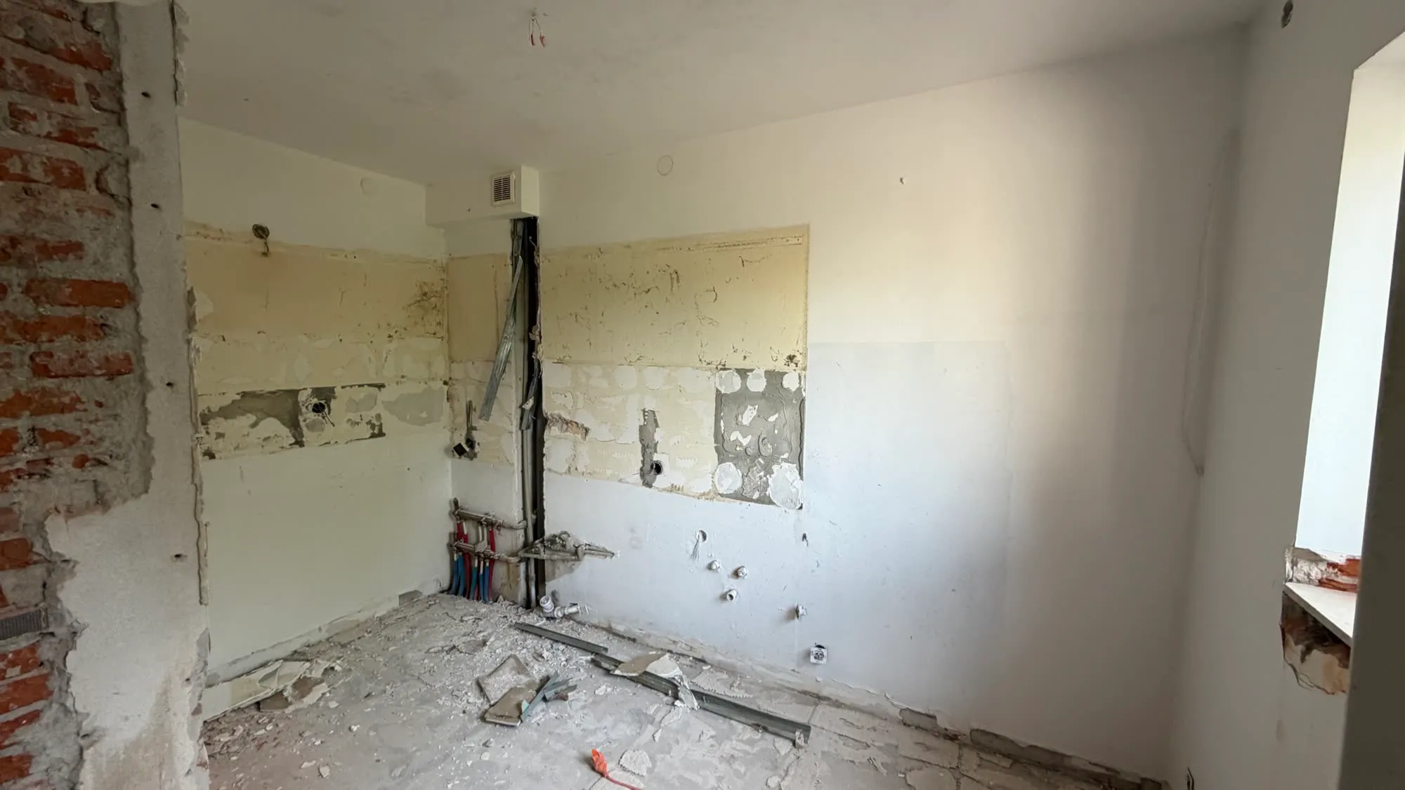Ściana kuchni po zdjęciu pasa płytek, widoczna warstwa kleju i odsłonięta instalacja wodna oraz puszki elektryczne