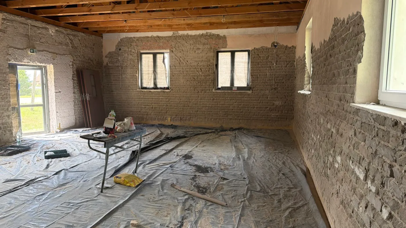 Sala ze ścianami skutymi do cegły, podłoga zabezpieczona folią, okna odsłonięte