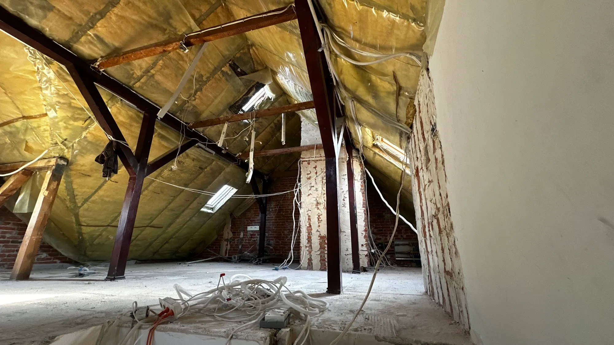 Poddasze z wełną mineralną między krokwiami, drewniana więźba dachowa i ceglany szczyt